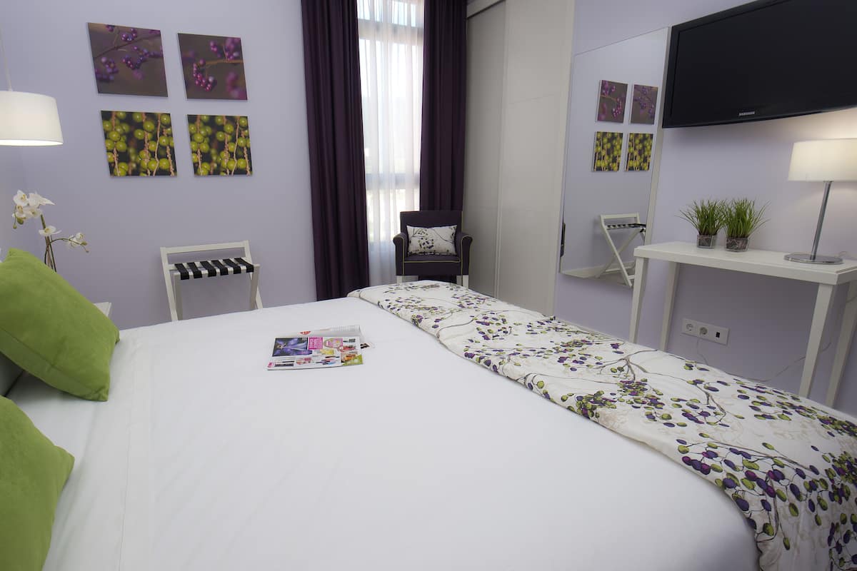 A neatly arranged hotel room with a bed, a chair, a desk, and a TV.