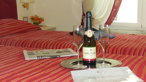 A hotel room with a bed, a bottle of wine, two wine glasses, and a menu. - Locanda Colosseo (Rome)