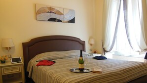 A hotel room with a bed, a bedside table with a lamp, a bottle of wine, two glasses, a book, and a painting on the wall. - Locanda Colosseo (Rome)