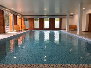 An indoor swimming pool with tiled flooring, wooden benches, and large windows. - Bahía Montaña (Villa La Angostura)