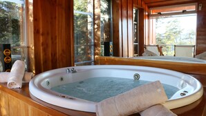 Interior de una cabaña de madera con jacuzzi, paredes de madera y ventanas amplias.