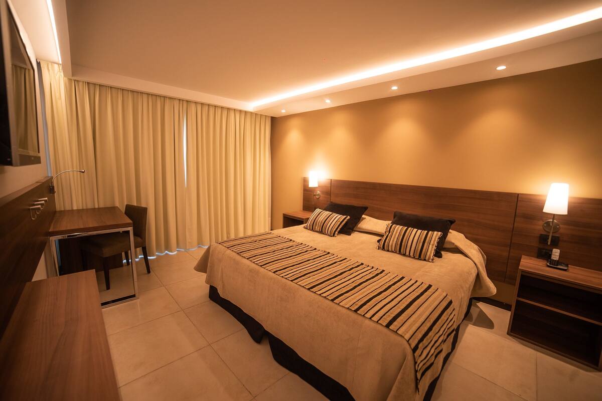 A hotel room with a large bed, bedside tables, a desk, and a mirror.