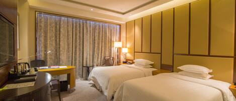A hotel room with two beds, a desk, and a television.