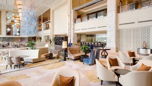 A spacious lobby with a high ceiling, chandeliers, seating areas, and a bar. - Sheraton Qingdao Jiaozhou Hotel (Qingdao)