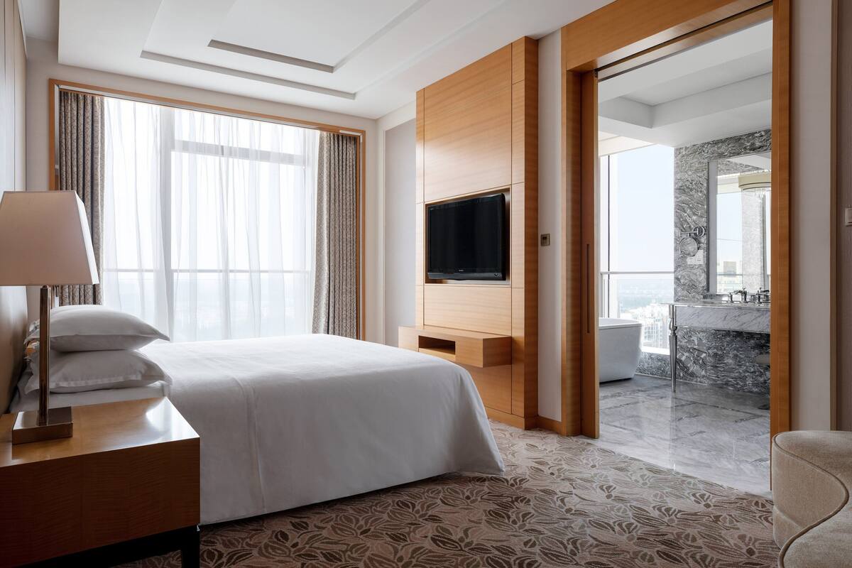 Ein Hotelzimmer mit einem großen Bett, einem an der Wand montierten Fernseher und einem durch eine offene Tür einsehbaren Badezimmer.