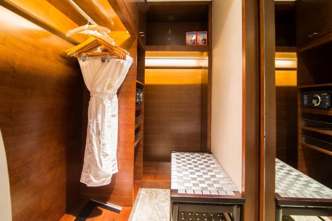 A narrow, wooden-finished bathroom with a towel rack, a small step, and a microwave.