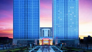 A modern hotel with a prominent entrance and two tall buildings in the background. - Sheraton Qingdao Jiaozhou Hotel (Qingdao)