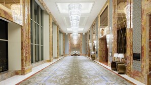 A luxurious hallway with a patterned carpet, marble walls, and a large chandelier. - Sheraton Qingdao Jiaozhou Hotel (Qingdao)