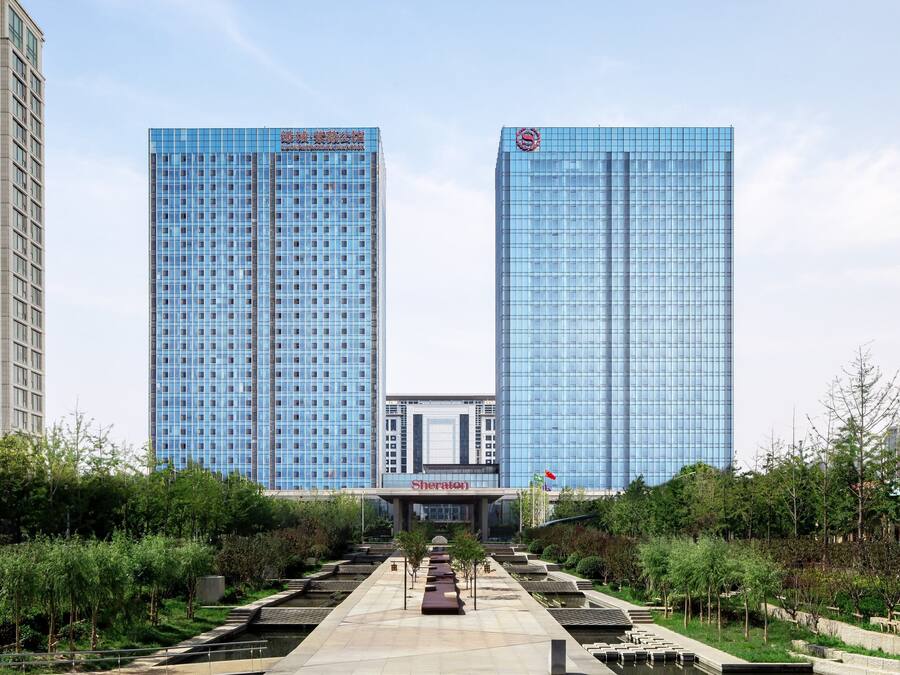 Un hotel con facciata in vetro moderna, ingresso centrale e un'area giardino curata di fronte.
