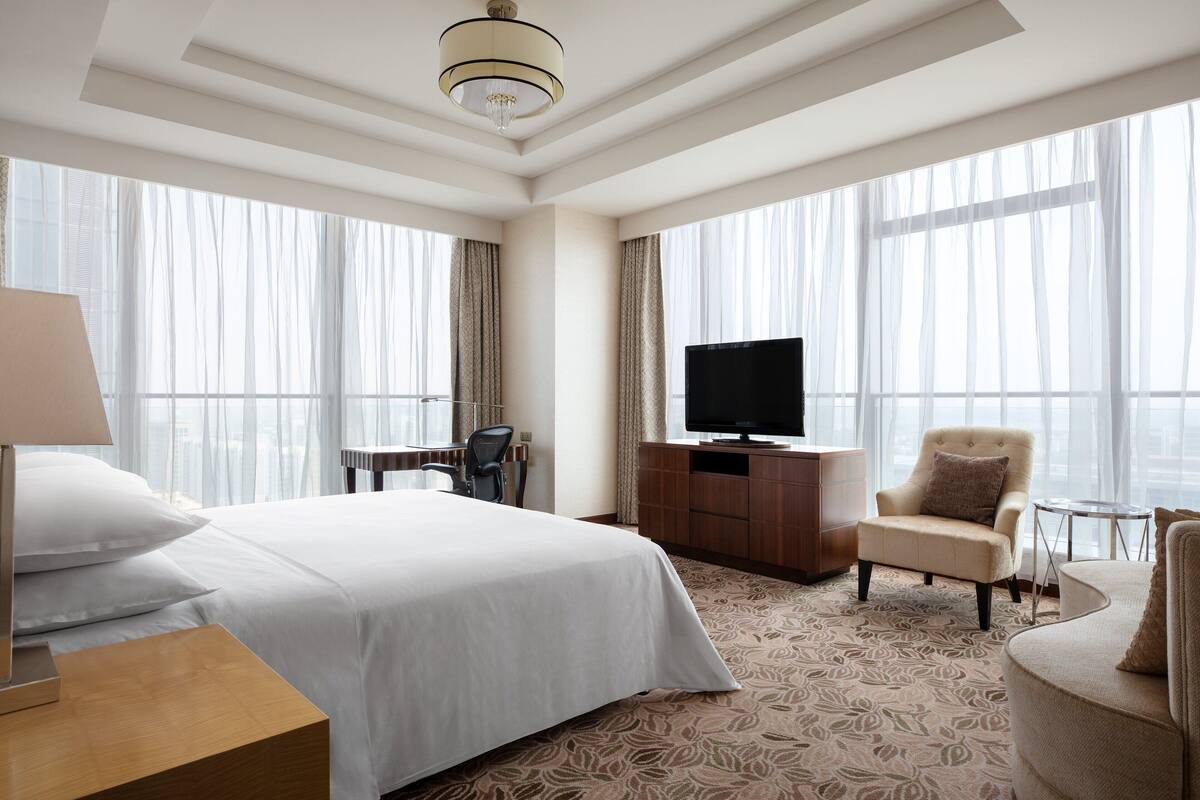 Ein Hotelzimmer mit einem großen Bett, einem Fernseher, einem Schreibtisch und einem Sessel.