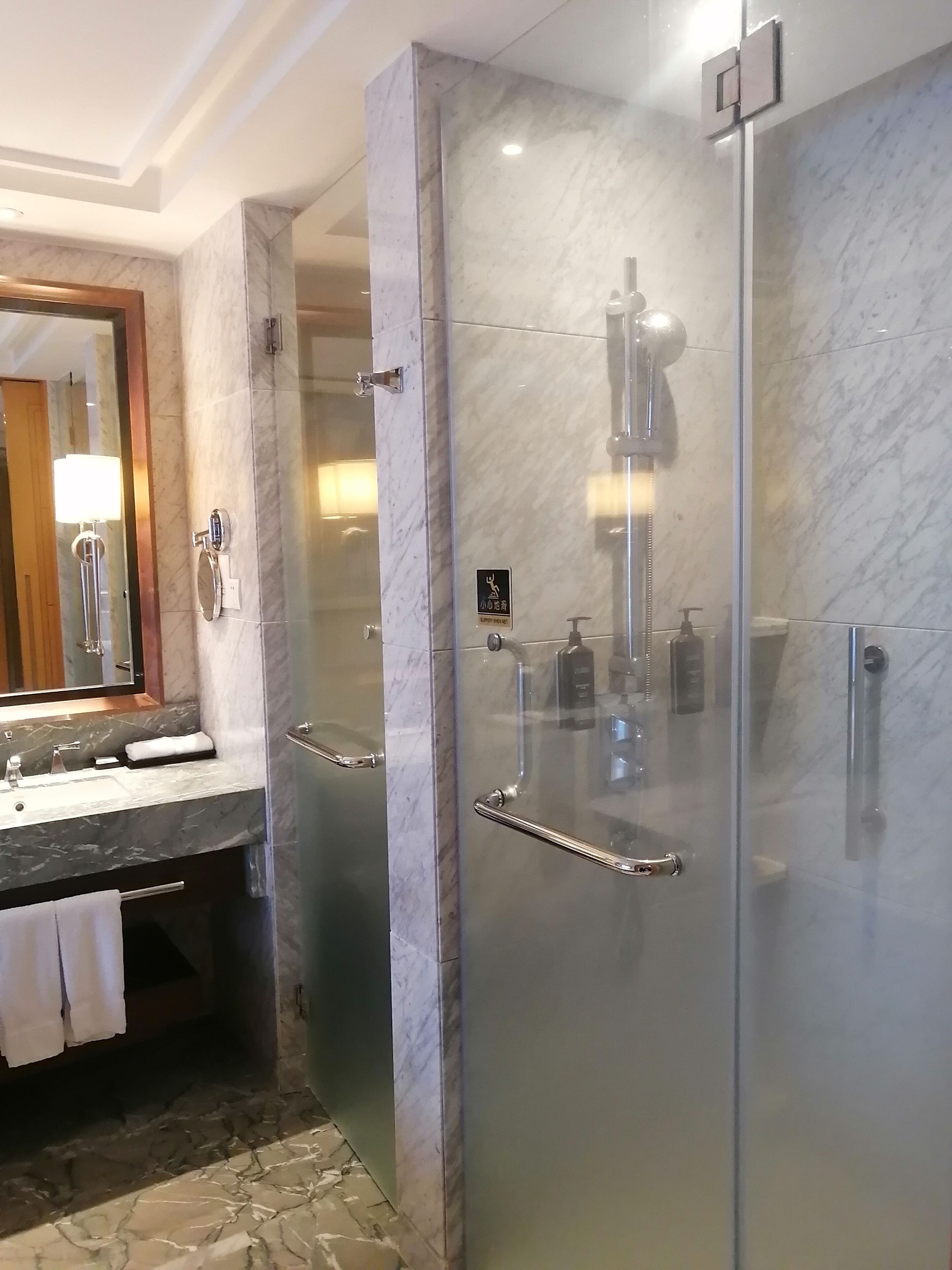 A modern bathroom with a glass-enclosed shower, a marble sink, and a vanity with a towel rack.