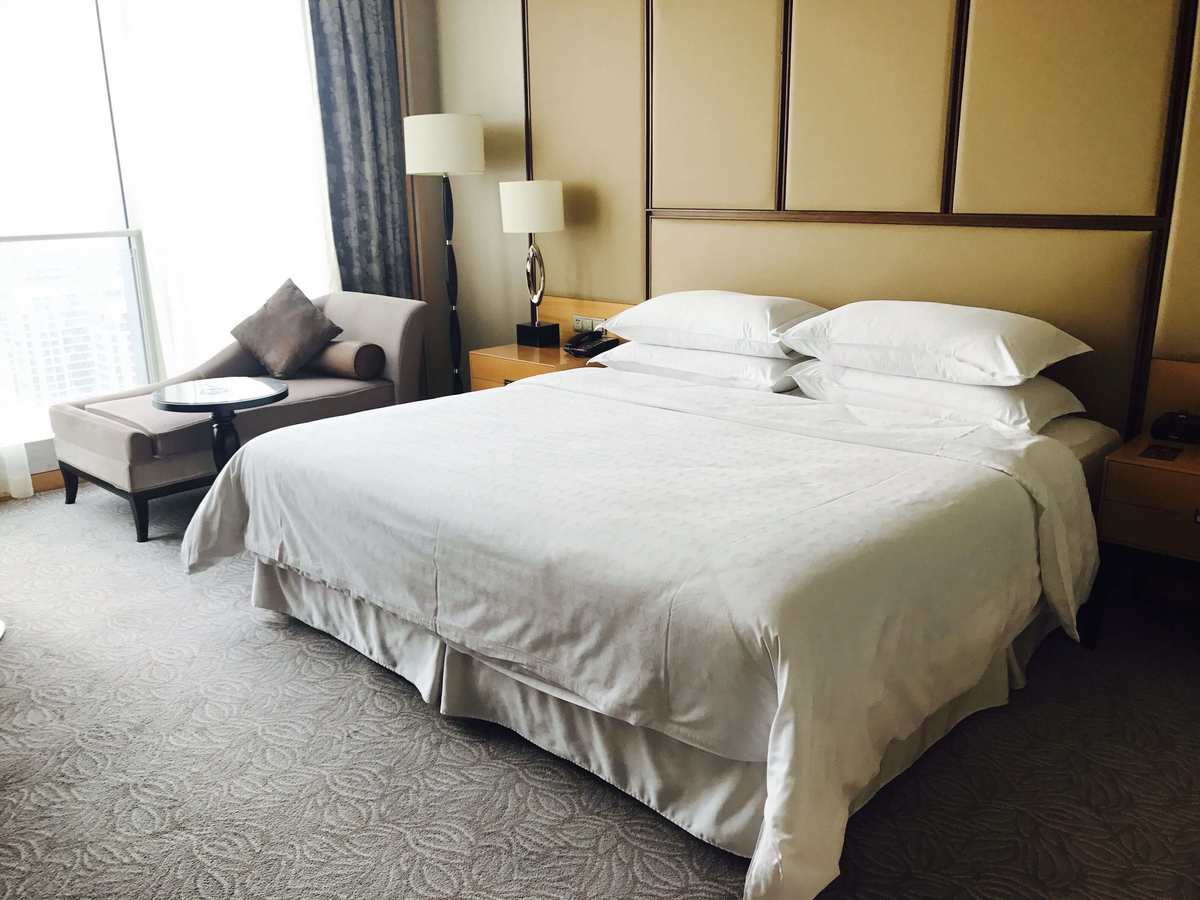 A hotel room with a large bed, a chair, a nightstand, and a lamp.
