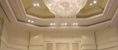 Una sala elegante con un gran candelabro, una pared larga con paneles verticales y una consola con lámparas.