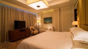 A hotel room with a large bed, a television on a wooden cabinet, a desk with a lamp, and a painting on the wall.