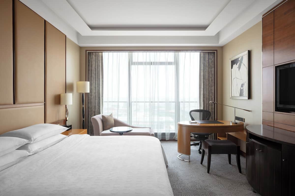 A hotel room with a bed, desk, chair, and TV.