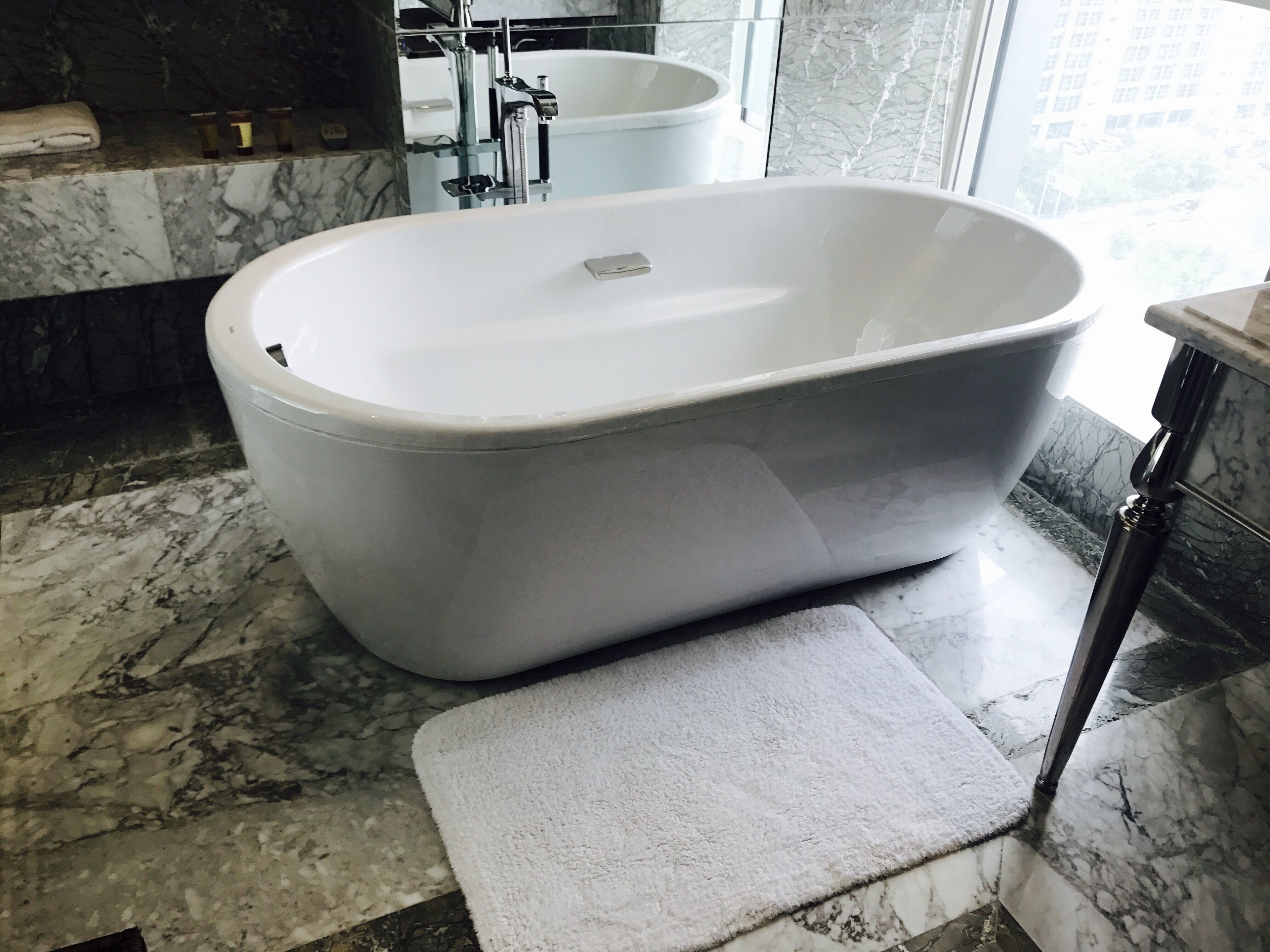 A modern bathroom with a freestanding bathtub, marble flooring, and a large window providing natural light.