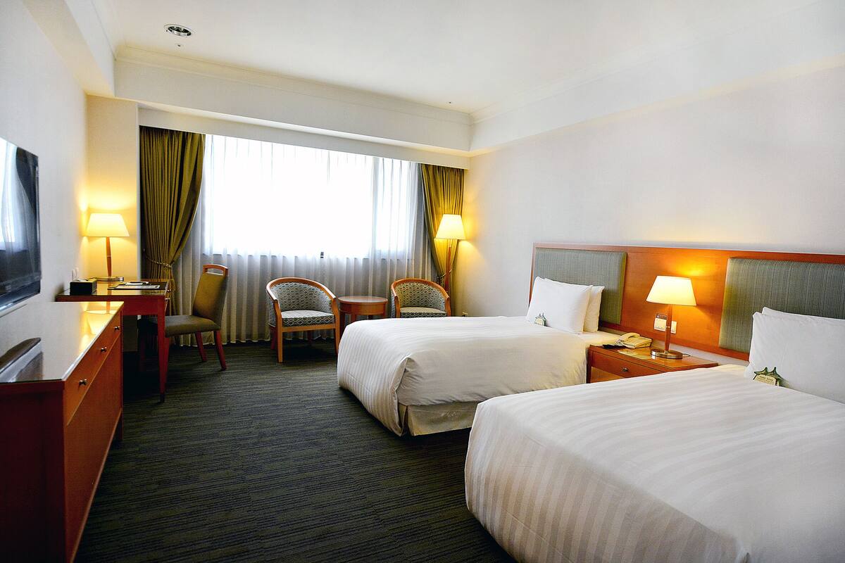Une chambre d’hôtel avec deux lits, un bureau, une chaise et un téléviseur.