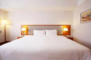 A hotel room with a large bed, two bedside lamps, a nightstand with a phone, and a painting on the wall.