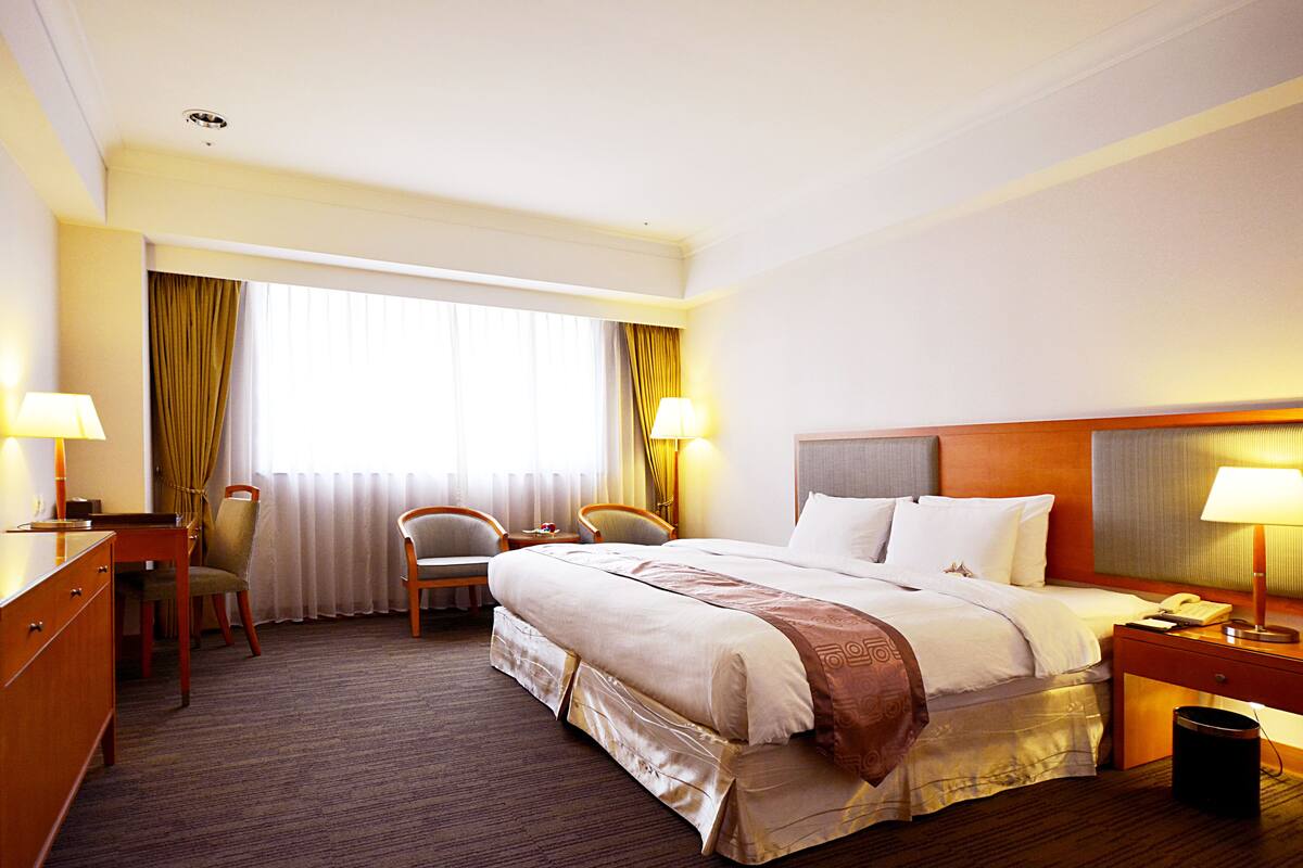 Une chambre d’hôtel avec un grand lit, deux chaises, un bureau et une table de chevet avec une lampe.