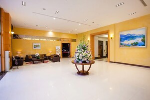 A spacious lobby with a polished floor, a reception desk, seating area, and a large floral arrangement.