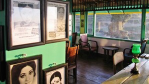 A cozy interior with framed pictures on the wall, wooden chairs, a small table, and a green lamp. - Te Aroha Dhanachuli (Dhari)
