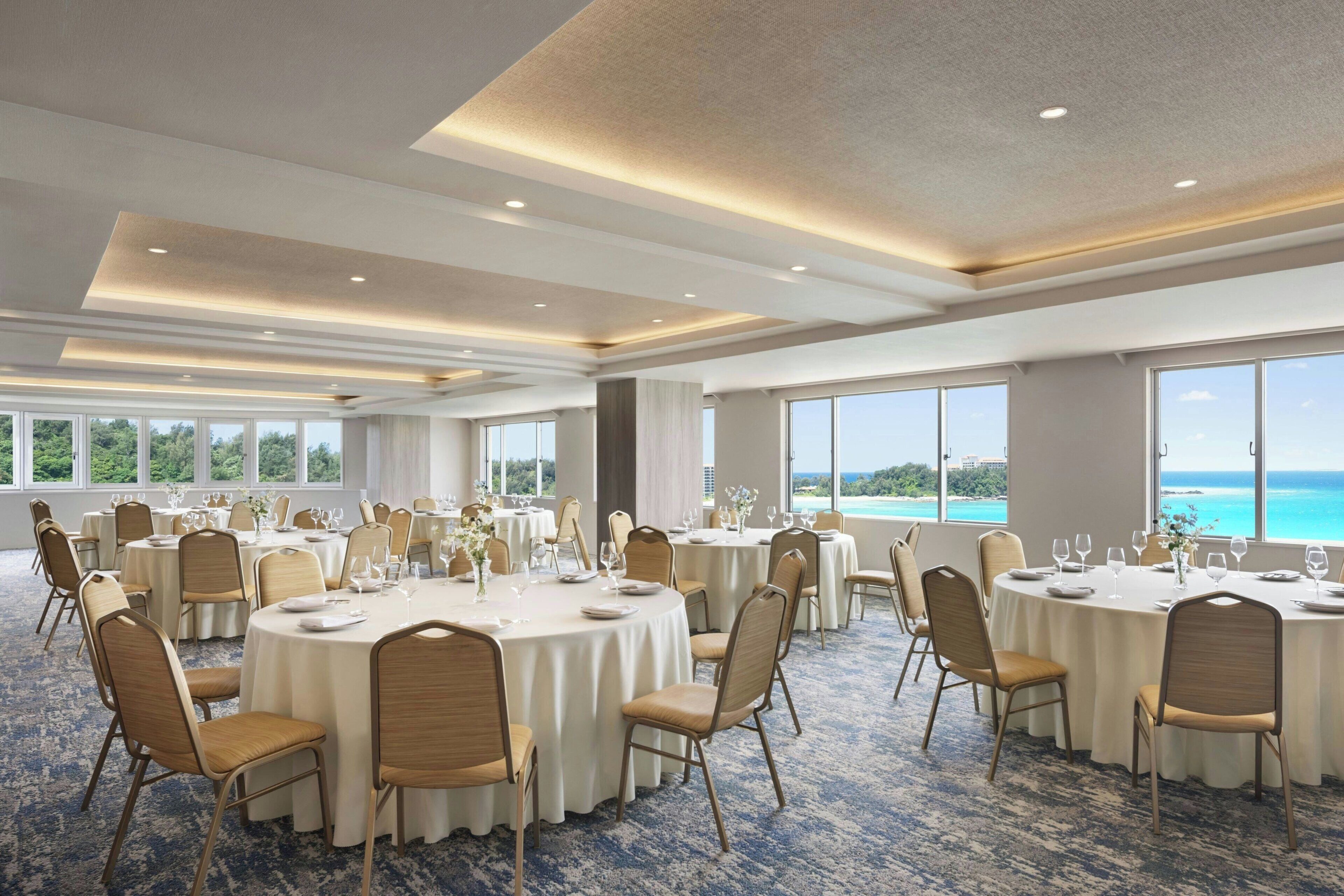 A large conference room with round tables, chairs, and a view of the ocean.