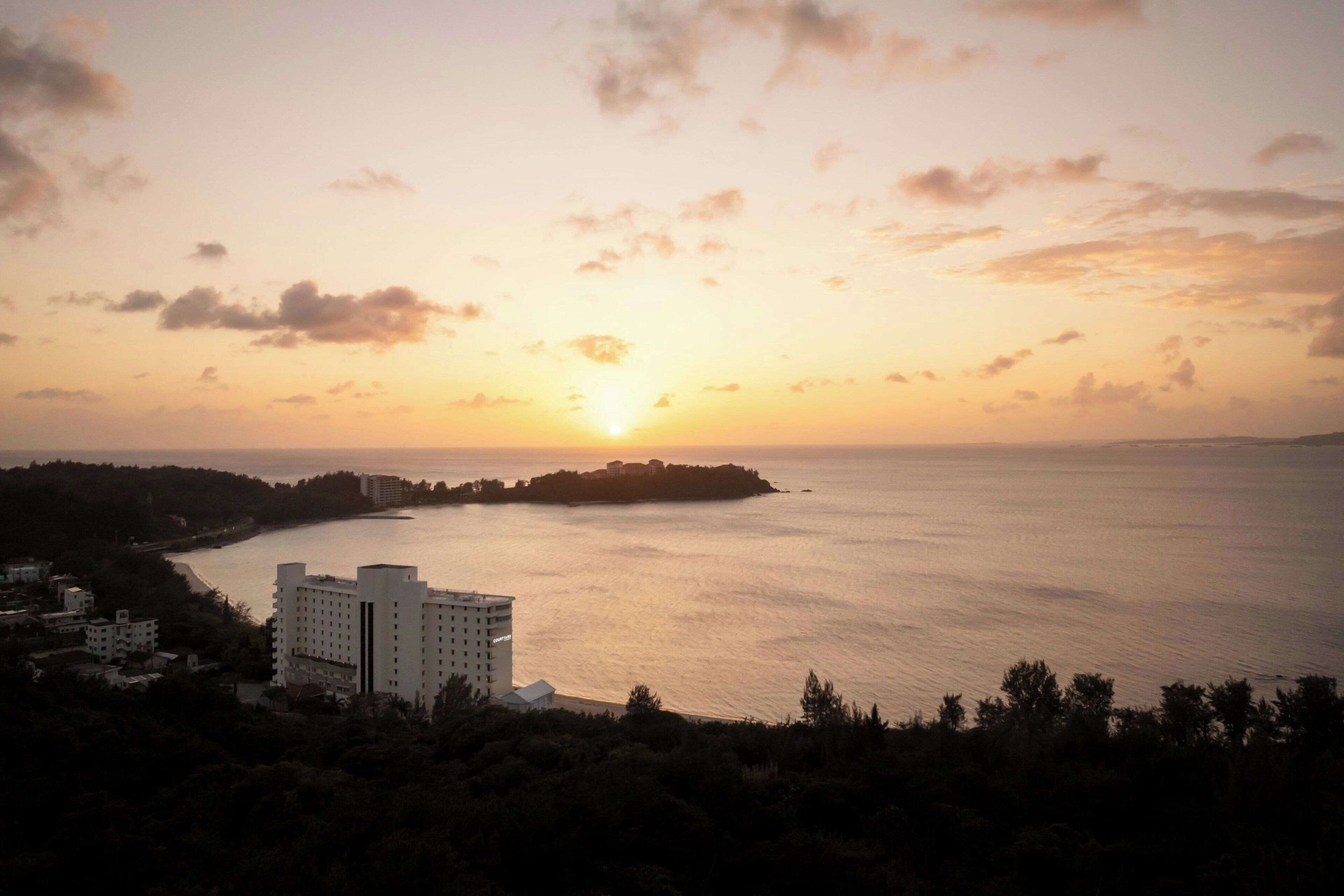 Vista costera con un edificio cerca del agua, cielo despejado y un atardecer.
