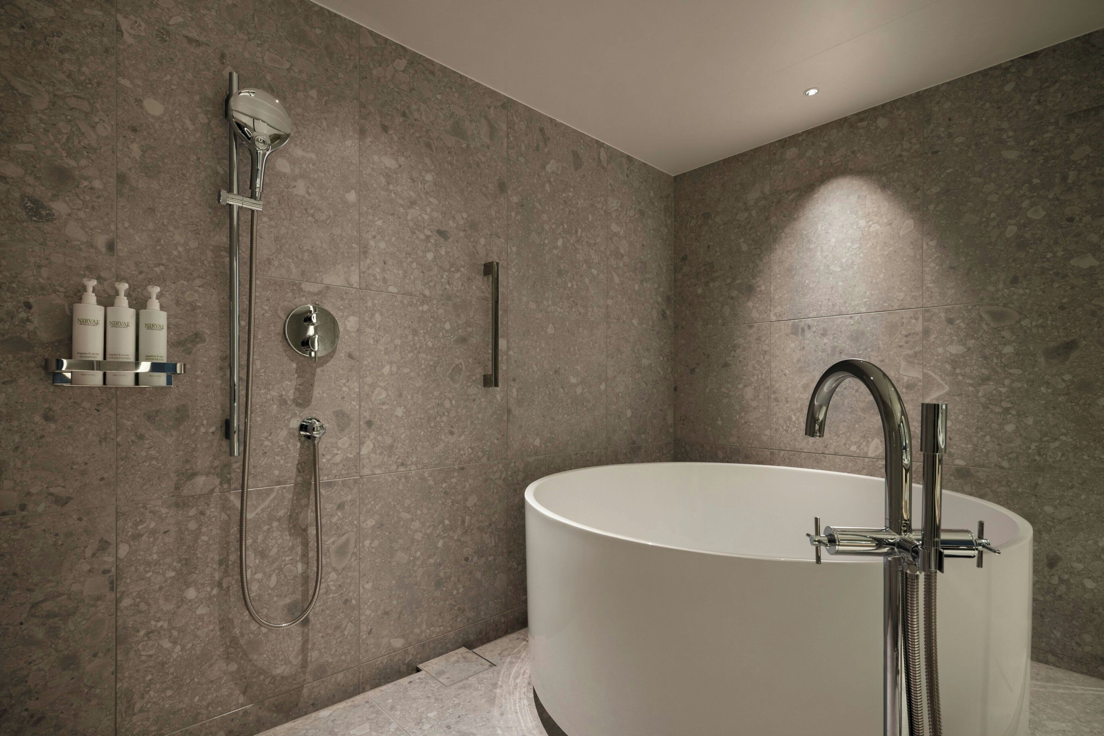 A modern bathroom with a freestanding bathtub, a handheld showerhead, and a wall-mounted faucet.