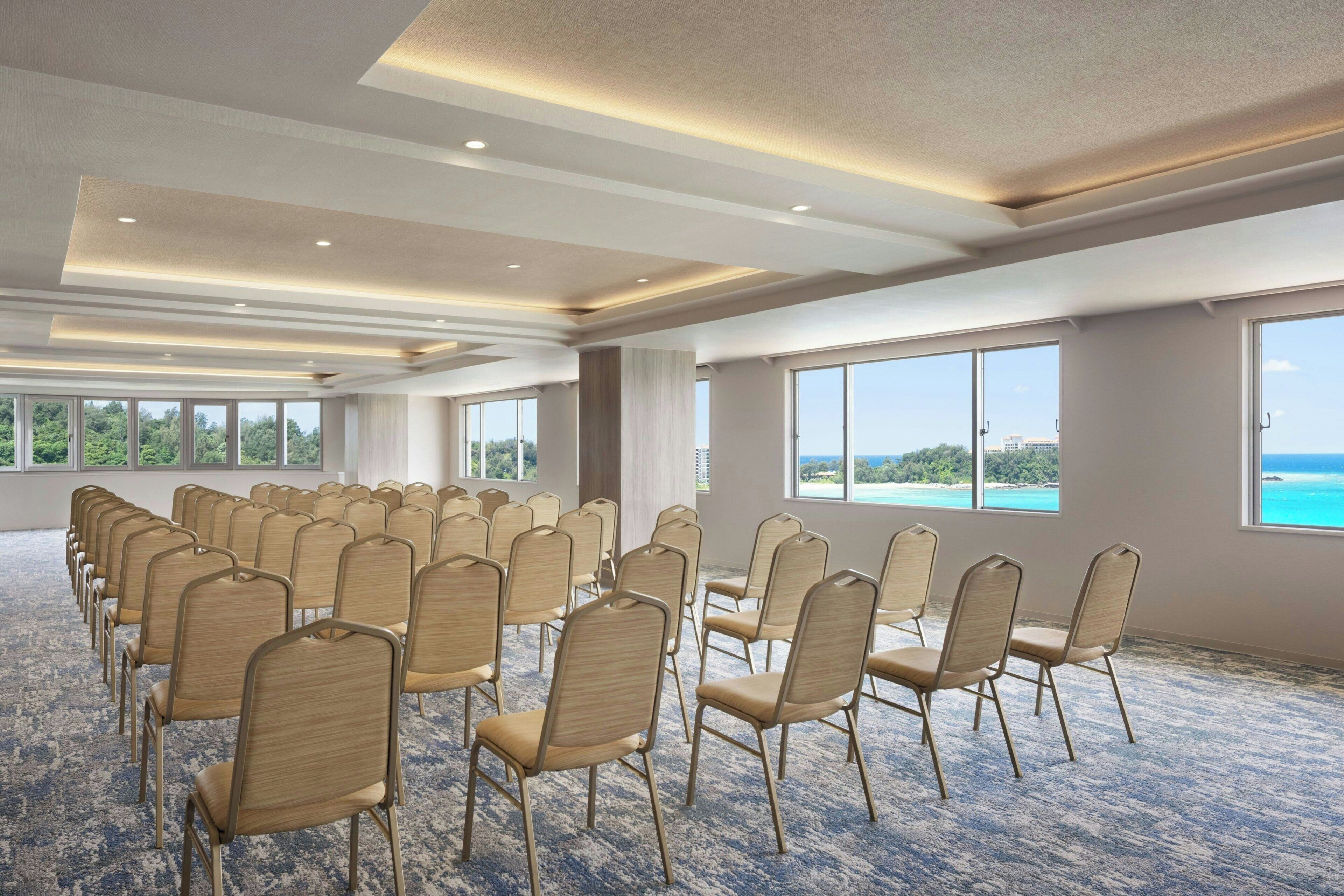 A conference room with rows of chairs, large windows, and a carpeted floor.