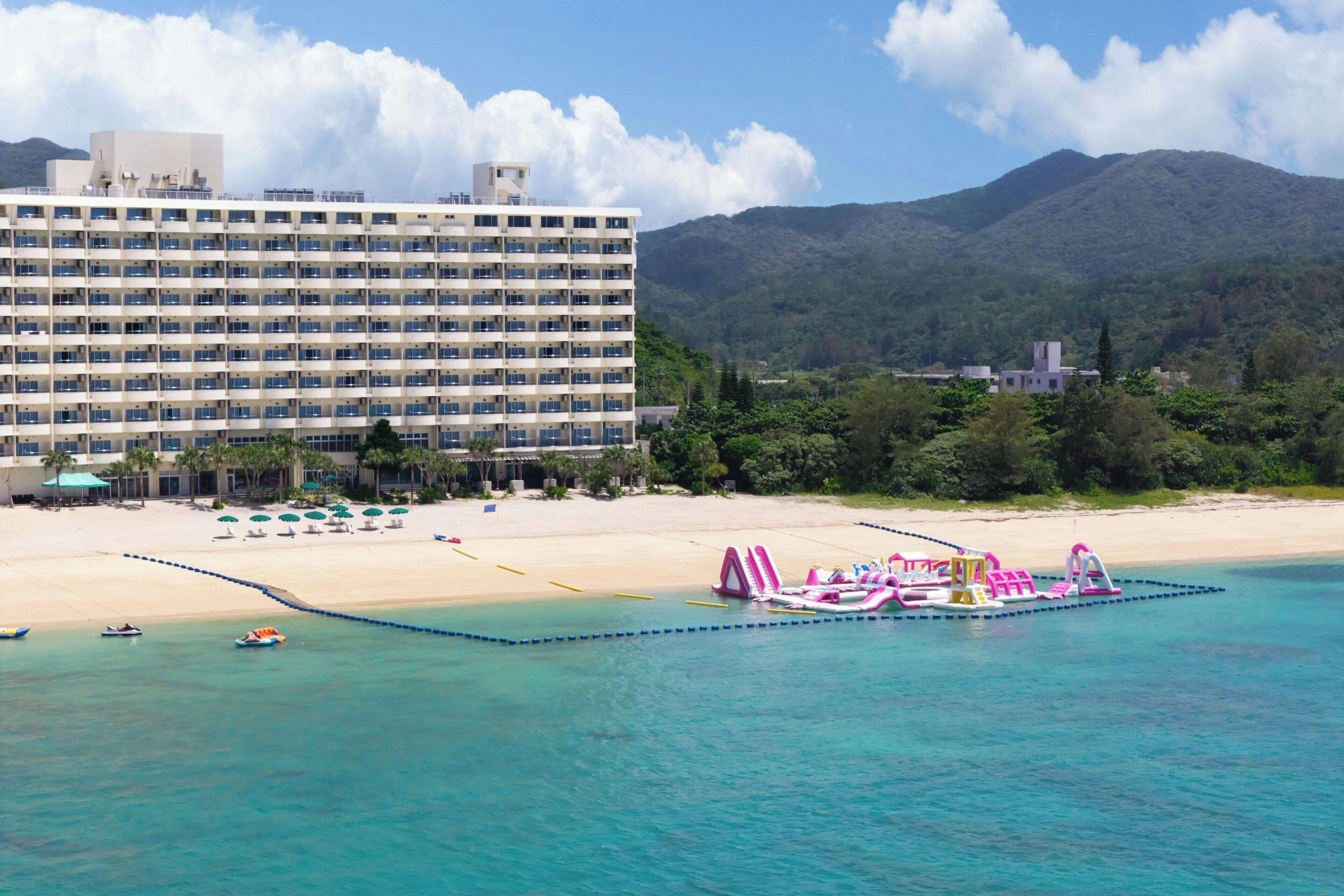 Um hotel à beira-mar com um edifício grande, uma praia arenosa e um mar azul cristalino.