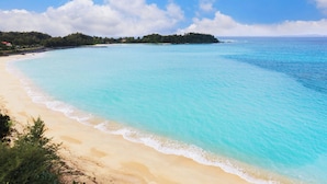 A beach with clear turquoise water, a sandy shore, and a distant tree-covered island. - Courtyard by Marriott Okinawa Resort (Nago)