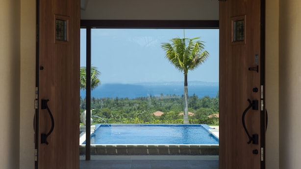 An open doorway leading to a pool with a view of a mountain range and palm trees. - Kanehide Kise Country Club (Nago)
