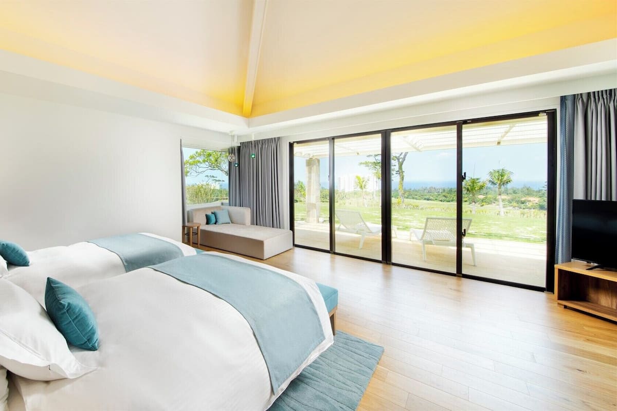 A modern bedroom with a large bed, a sofa, a TV, and a balcony with a view.