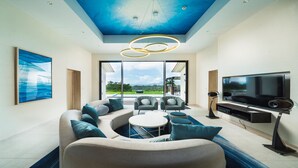 A modern living room with a large sofa, a TV, and a ceiling with a blue design. - Kanehide Kise Country Club (Nago)
