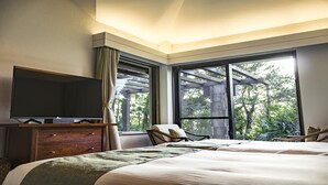 A hotel room with a large bed, a TV on a wooden dresser, and a view of trees through large windows. - Kanehide Kise Country Club (Nago)
