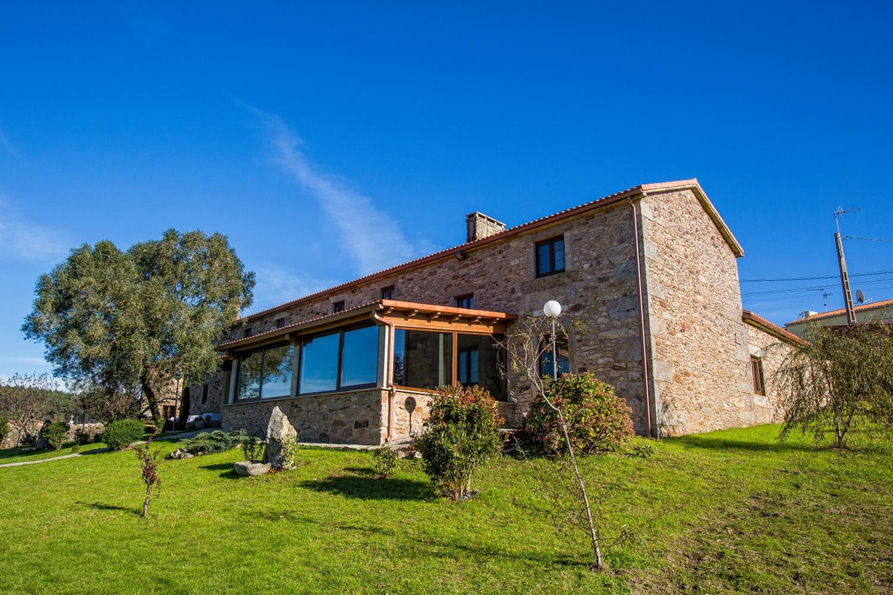 Una casa de piedra con un amplio ventanal, una pérgola y un césped bien cuidado.