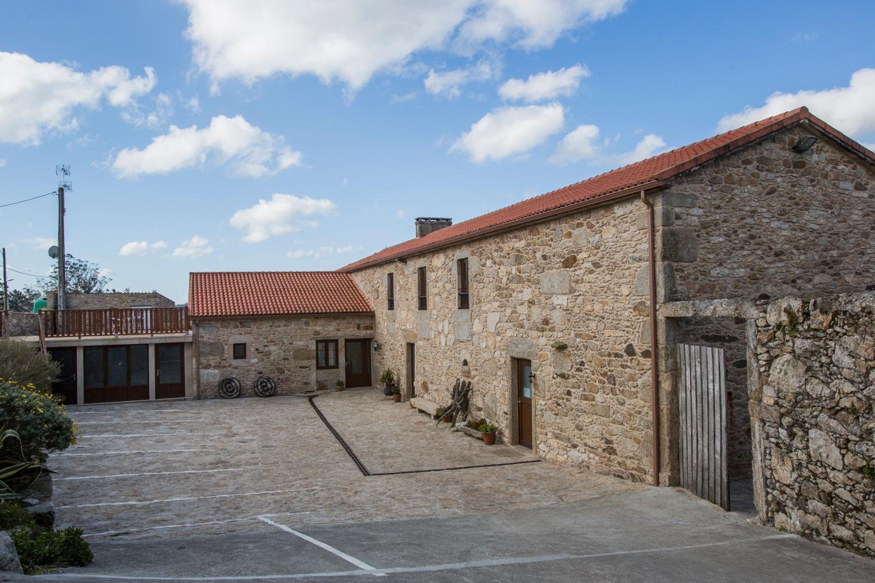 Un bâtiment en pierre avec un toit recouvert de tuiles rouges, une cour avec une zone pavée et un portail en bois.