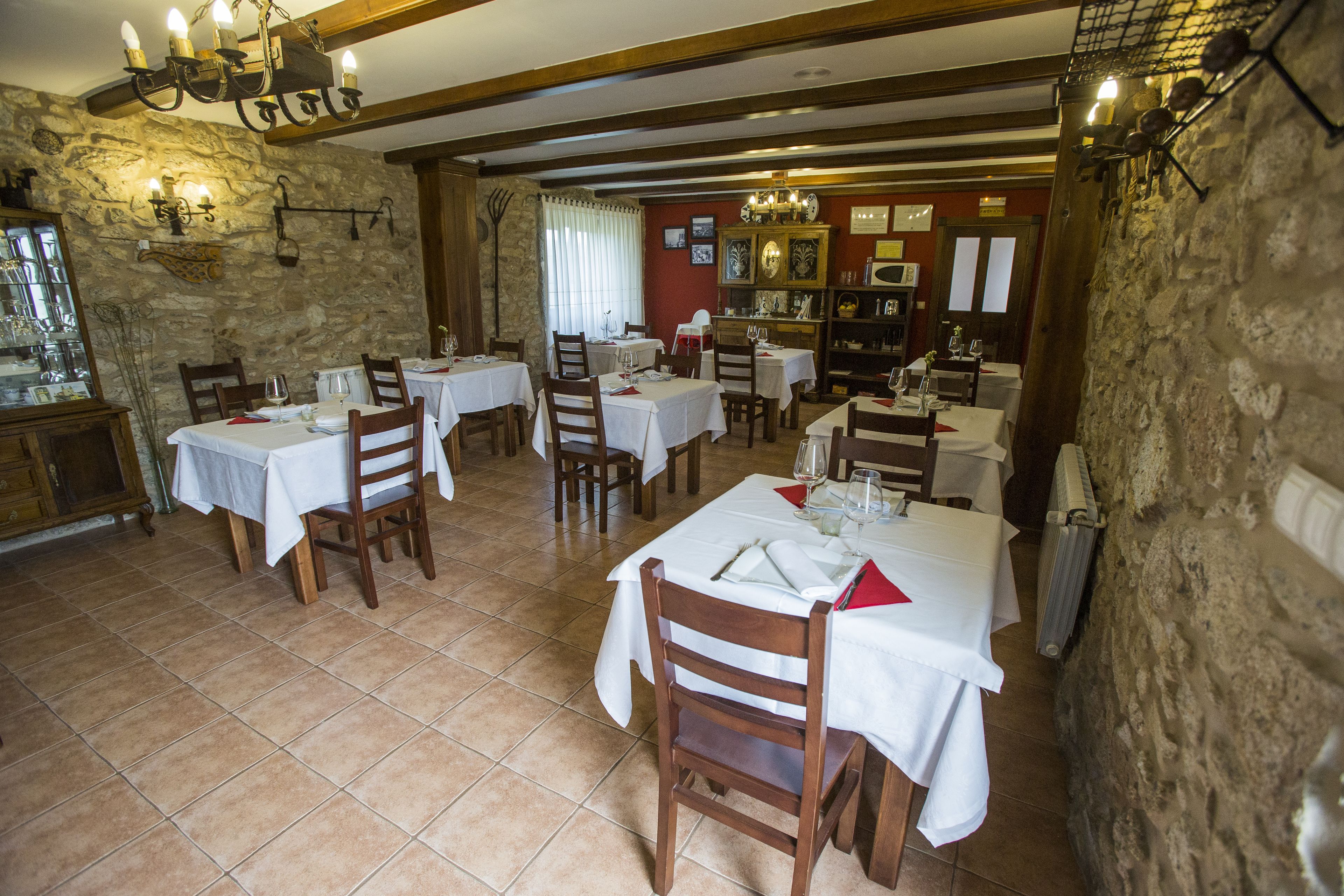 Restaurante com várias mesas e cadeiras, paredes de pedra e um lustre.