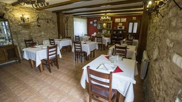 Restaurante com várias mesas e cadeiras, paredes de pedra e um lustre.