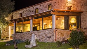 A stone building with large windows and a covered patio area. - Casa Castiñeira (Muxía)