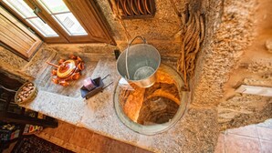A rustic kitchen with a stone wall, a hanging pot rack, and a large pot on the counter. - Casa Castiñeira (Muxía)