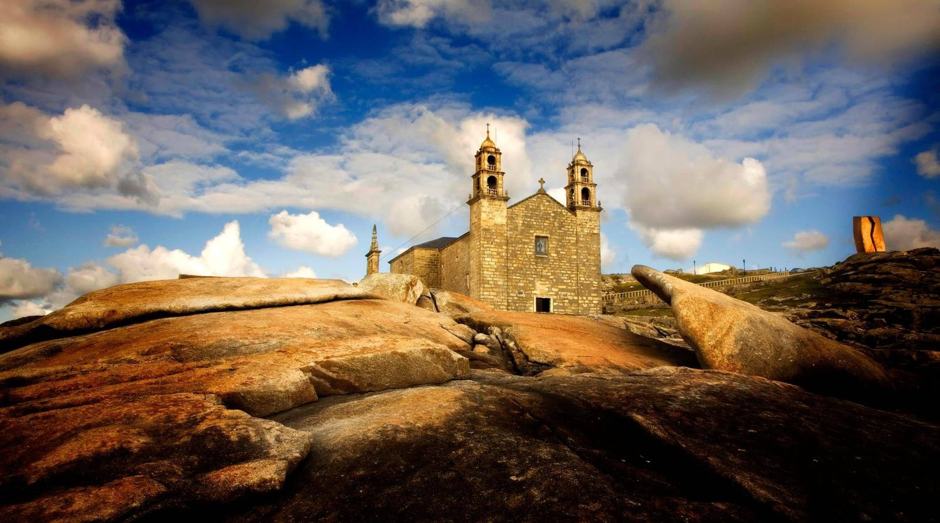 Eine steinerne Kirche mit zwei Türmen vor blauem Himmel mit Wolken.