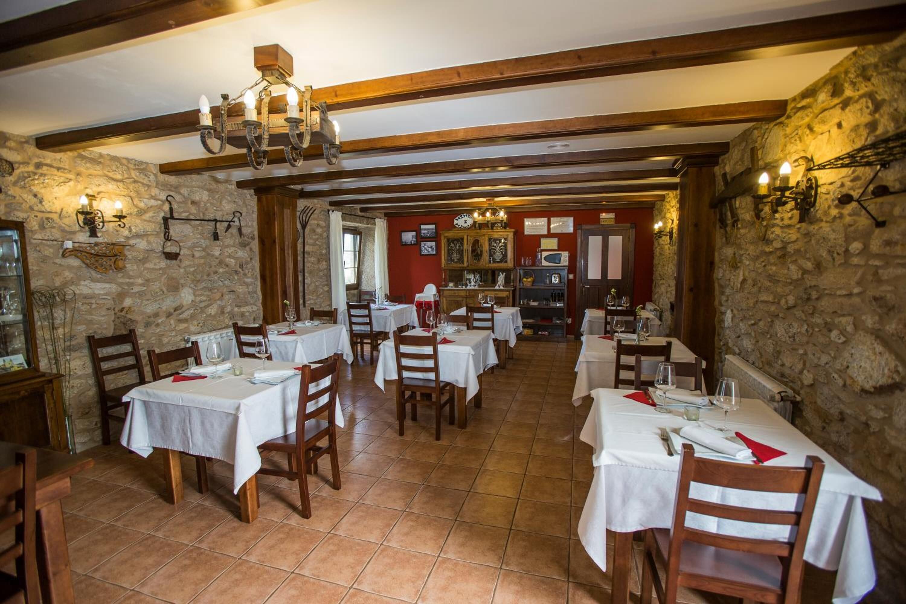 Un restaurante con varias mesas, vigas de madera, paredes de piedra e iluminación colgante.