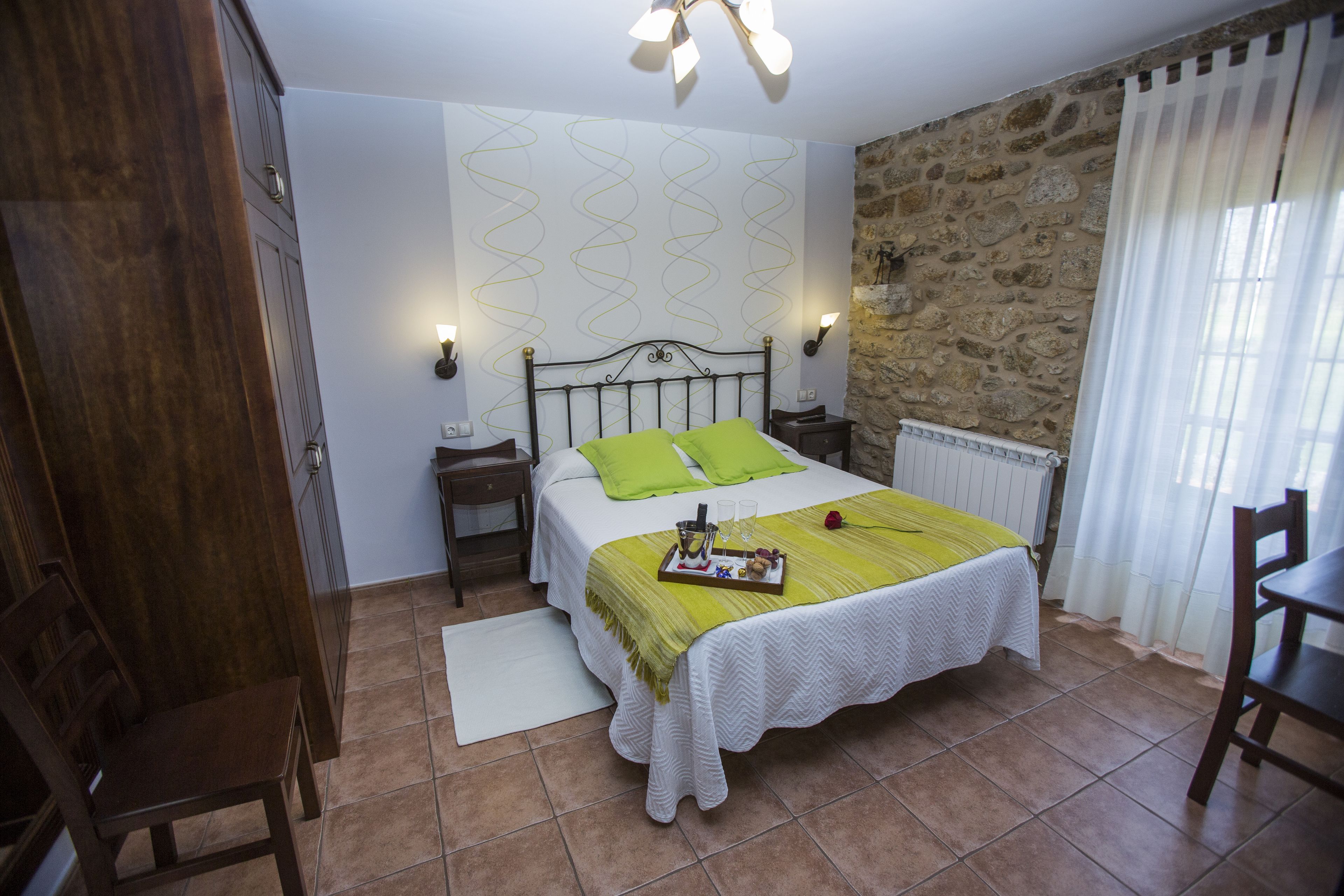 Een slaapkamer met een bed, nachtkastje, dressoir, stoel en een stenen muur.