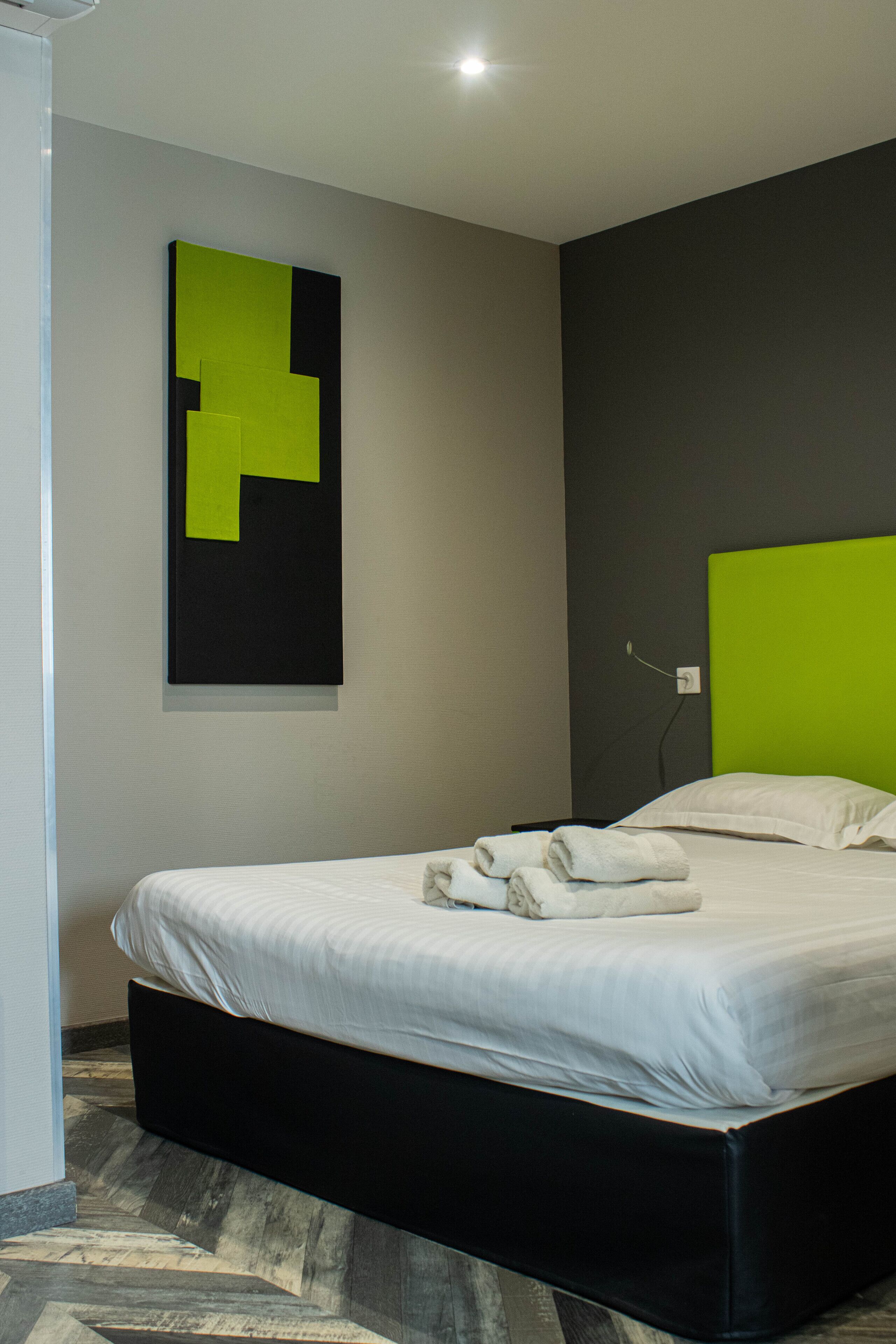 A modern hotel room with a large bed, a green accent wall, and a geometric art piece above the bed.