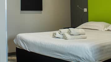 A modern hotel room with a large bed, a green accent wall, and a geometric art piece above the bed.
