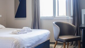 Una habitación de hotel moderna con una cama grande, una silla, un escritorio y una ventana con cortinas.