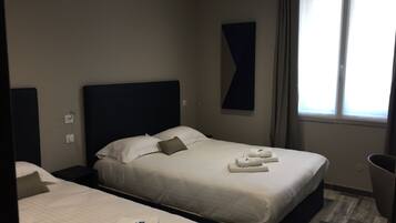 Habitació d'hotel amb dos llits, un capçal de llit fosc, una finestra gran amb cortines i una obra d'art abstracta penjada a la paret.