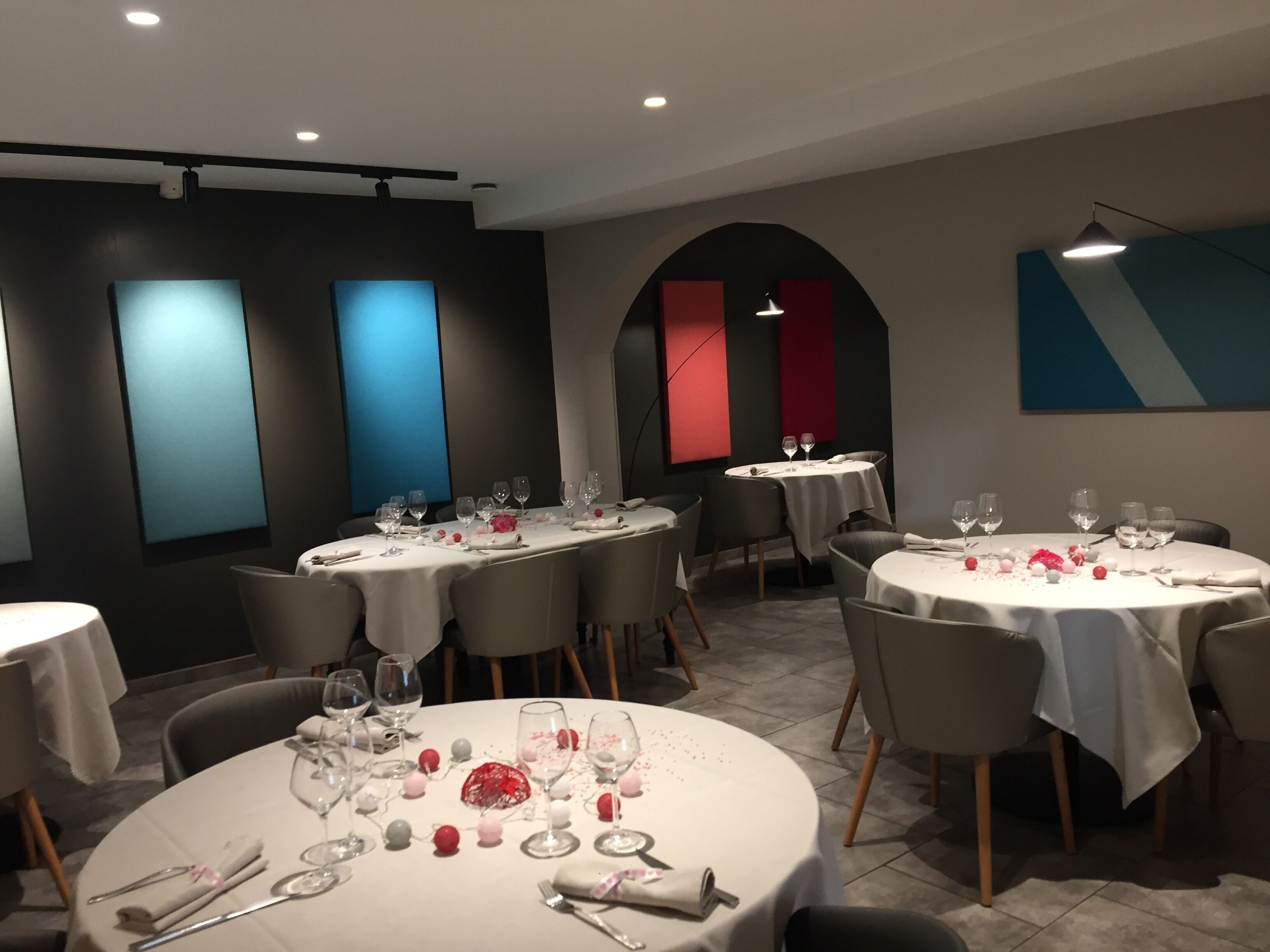 A modern dining area with round tables, each set with wine glasses and cutlery.
