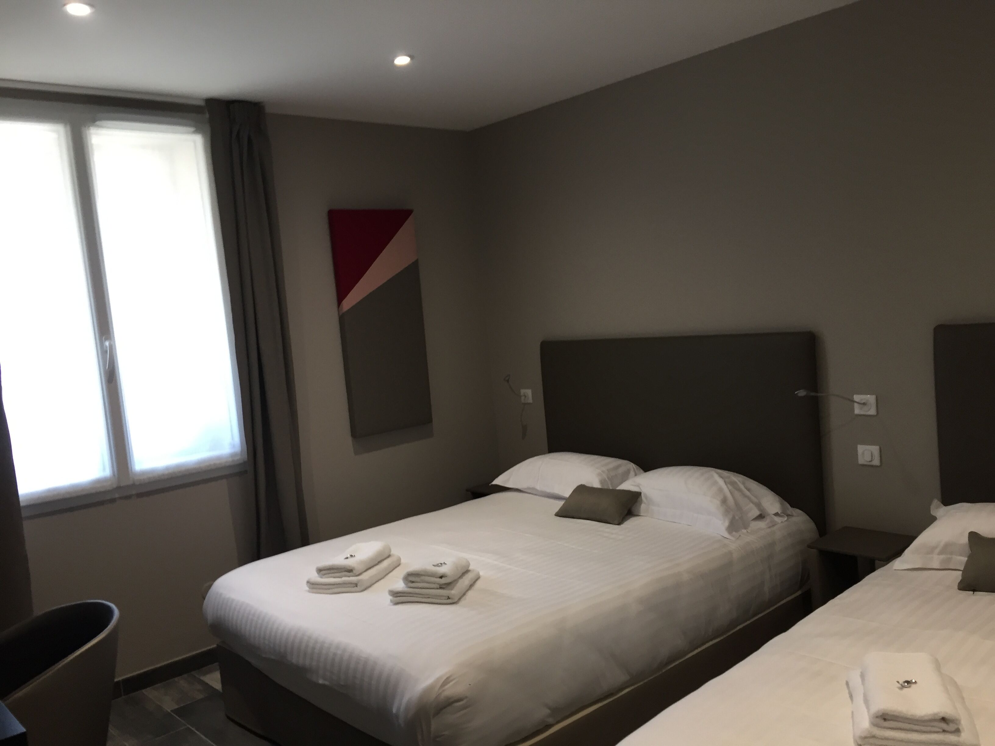 Et hotelværelse med to senge, et skrivebord og et vindue med gardiner.